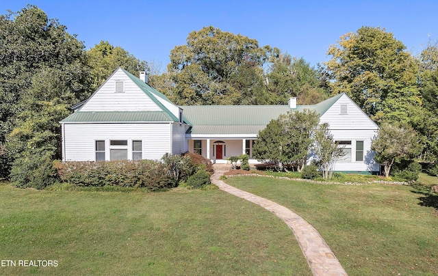 view of front facade featuring covered porch, metal roof, a chimney, and a front yard