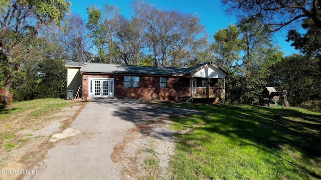 ranch-style home featuring french doors, a front yard, a playground, and a deck