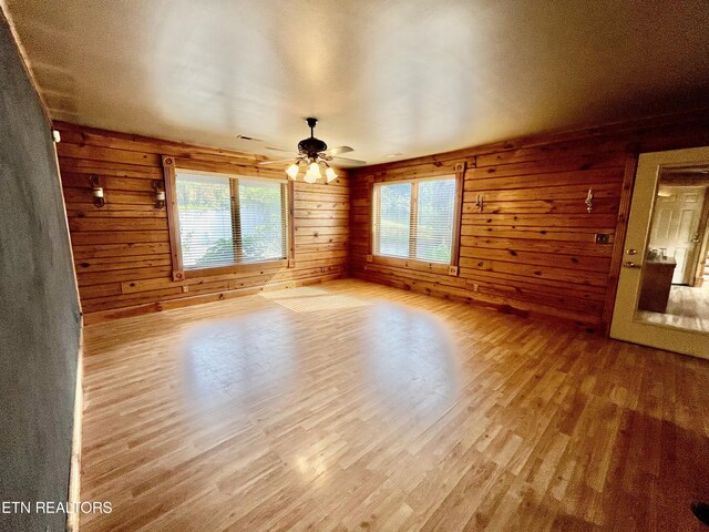 unfurnished room featuring wooden walls, ceiling fan, and hardwood / wood-style flooring