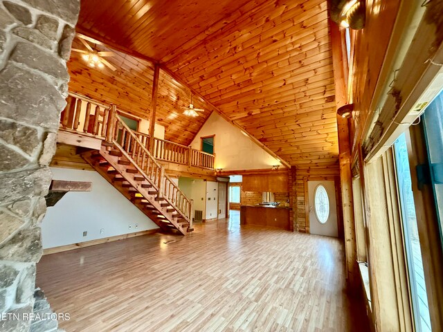 unfurnished living room with high vaulted ceiling, wooden ceiling, wood-type flooring, ceiling fan, and wooden walls