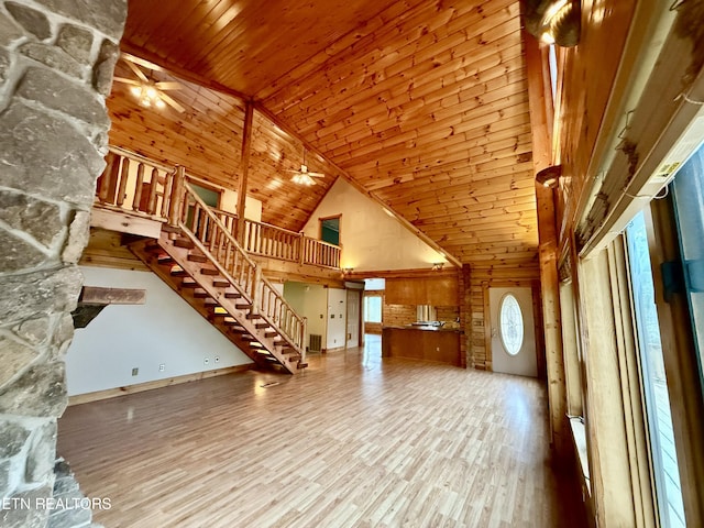 unfurnished living room with a ceiling fan, wood finished floors, high vaulted ceiling, and stairway