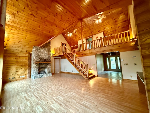 unfurnished living room with ceiling fan, a stone fireplace, hardwood / wood-style flooring, and high vaulted ceiling