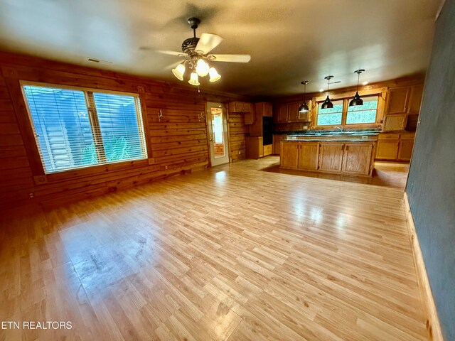 unfurnished living room featuring light wood-type flooring, wood walls, ceiling fan, and sink