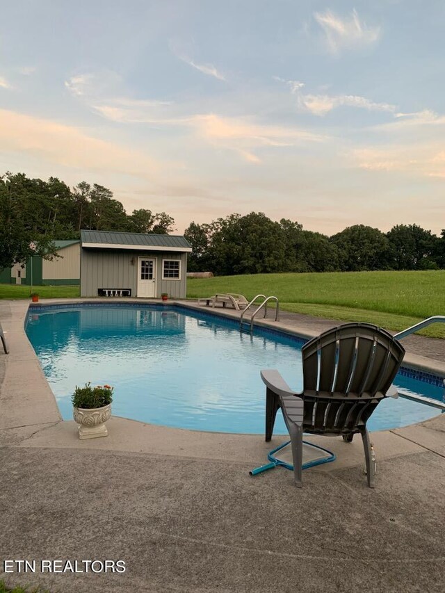 pool at dusk with a patio, an outbuilding, and a yard