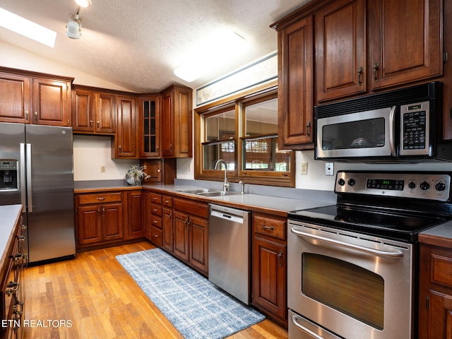 kitchen with lofted ceiling, sink, a textured ceiling, light hardwood / wood-style flooring, and appliances with stainless steel finishes