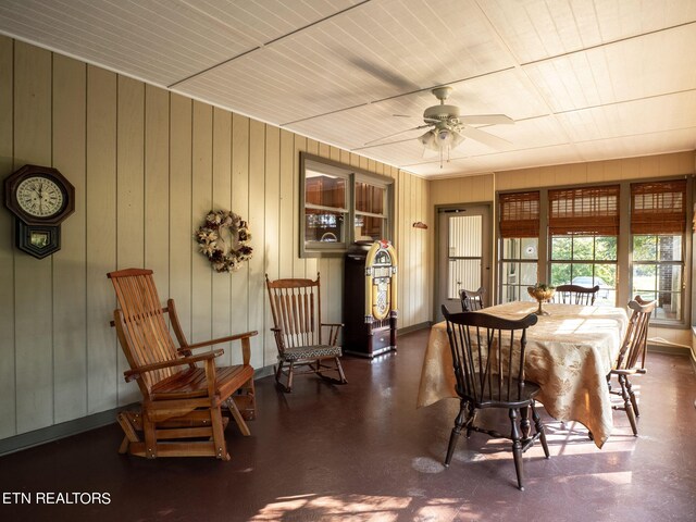 dining space with ceiling fan and wood walls