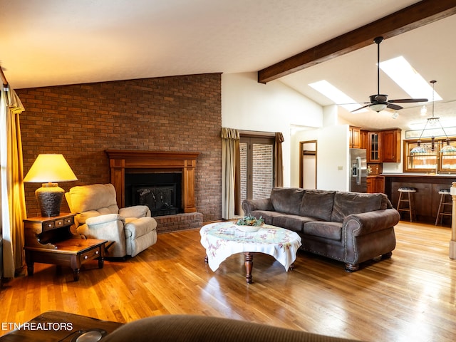 living room featuring light hardwood / wood-style flooring, ceiling fan, a fireplace, and lofted ceiling with skylight