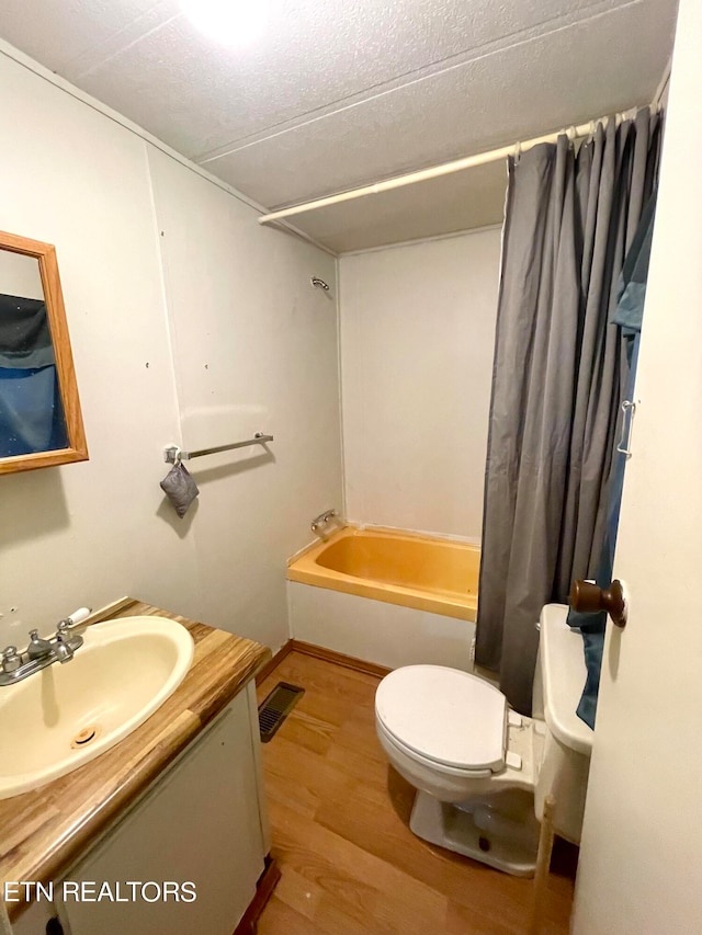 full bathroom featuring hardwood / wood-style floors, vanity, toilet, shower / bath combo, and a textured ceiling