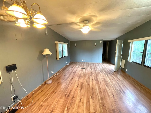 unfurnished living room featuring hardwood / wood-style flooring, ceiling fan with notable chandelier, vaulted ceiling, and a wealth of natural light