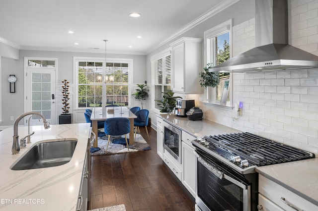 kitchen featuring appliances with stainless steel finishes, wall chimney exhaust hood, pendant lighting, dark hardwood / wood-style floors, and sink