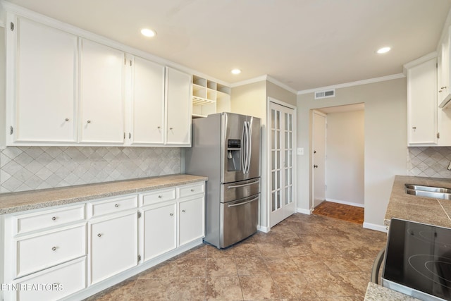 kitchen featuring white cabinets, stove, stainless steel fridge, and tasteful backsplash