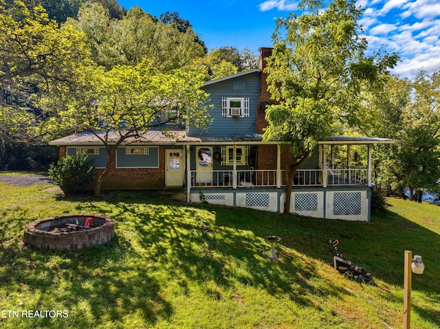 view of front of property featuring a front yard, brick siding, a fire pit, and a porch