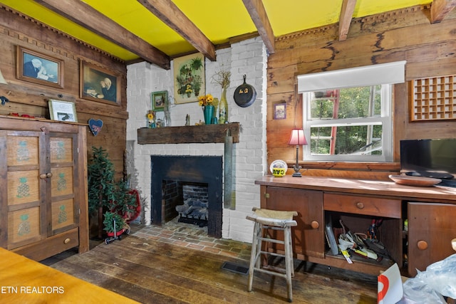 living room featuring a brick fireplace, beam ceiling, wood walls, and visible vents
