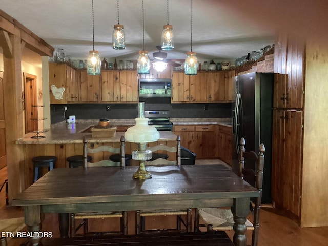 kitchen with a breakfast bar area, decorative light fixtures, brown cabinetry, and stainless steel appliances