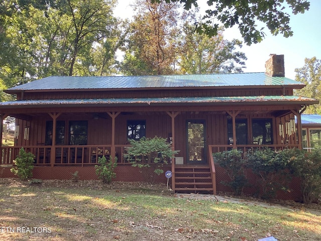 view of front of house featuring covered porch, a chimney, and metal roof