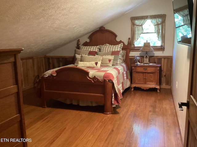 bedroom featuring hardwood / wood-style floors, lofted ceiling, a textured ceiling, and wood walls