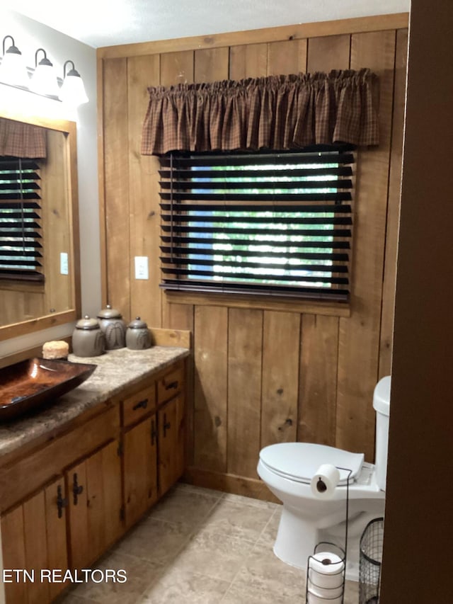half bath featuring toilet, vanity, and wood walls