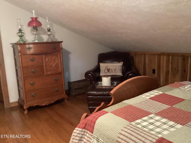 bedroom with a textured ceiling, wood walls, vaulted ceiling, and light wood-type flooring