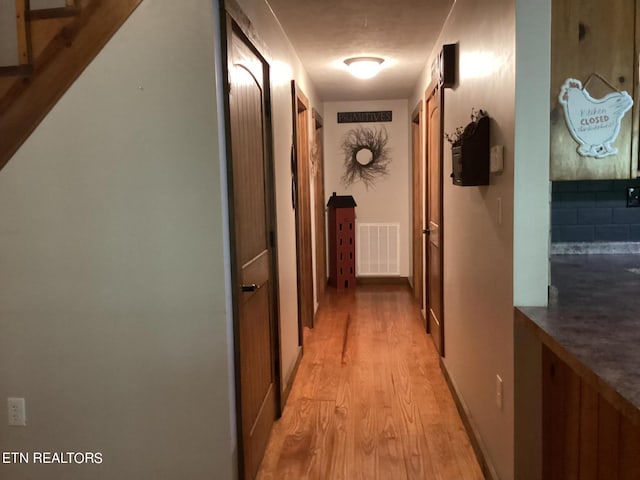 hallway with a textured ceiling and light hardwood / wood-style floors