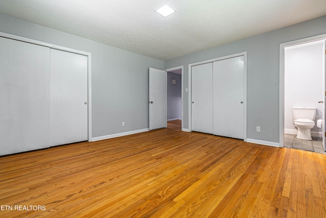 unfurnished bedroom with multiple closets, light wood-type flooring, and ensuite bathroom