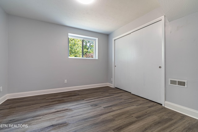 unfurnished bedroom featuring a textured ceiling, a closet, and dark hardwood / wood-style flooring