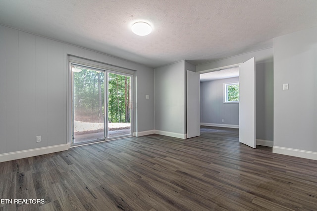 empty room featuring a textured ceiling, dark wood-style floors, and baseboards