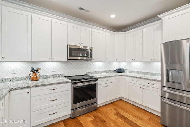 kitchen with white cabinetry, tasteful backsplash, light stone countertops, stainless steel appliances, and light hardwood / wood-style flooring