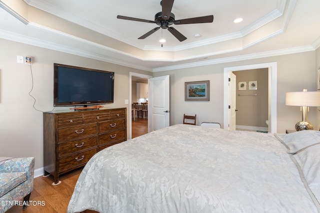 bedroom featuring ceiling fan, a tray ceiling, ornamental molding, and wood-type flooring