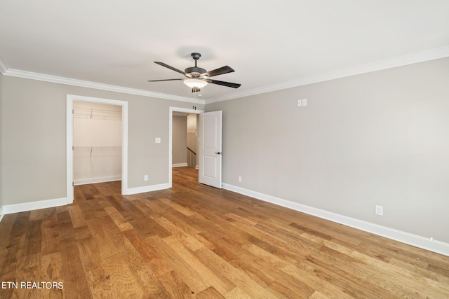 unfurnished bedroom featuring light hardwood / wood-style flooring, ceiling fan, a walk in closet, and crown molding