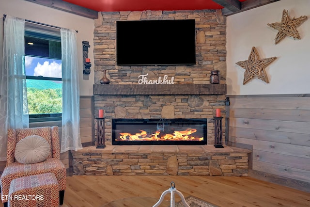 living room with a stone fireplace, beamed ceiling, and hardwood / wood-style flooring