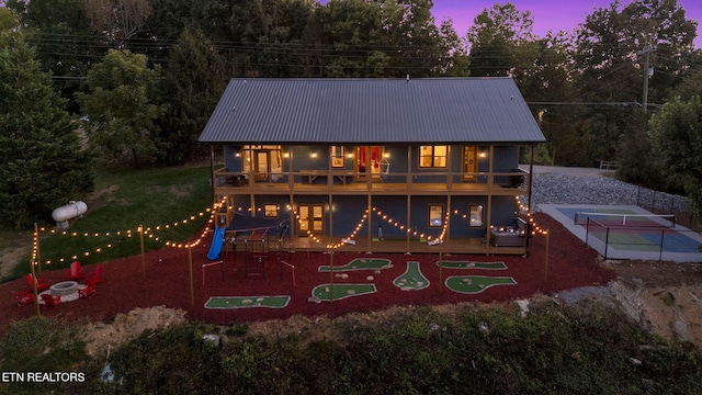 back house at dusk featuring a patio, a playground, a wooden deck, a yard, and a balcony