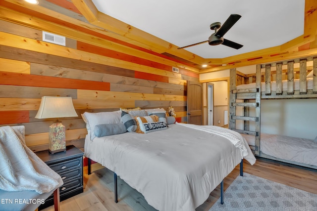 bedroom featuring light wood-type flooring, ceiling fan, and wood walls