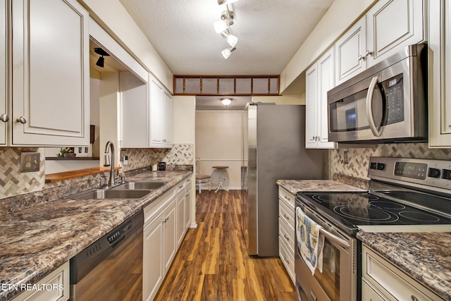 kitchen with dark hardwood / wood-style flooring, dark stone countertops, sink, stainless steel appliances, and a textured ceiling