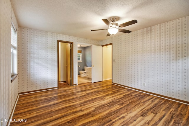 unfurnished bedroom with wood-type flooring, ensuite bathroom, a textured ceiling, and ceiling fan