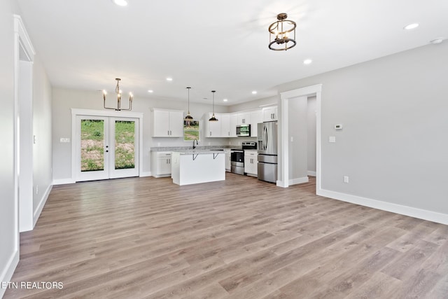 kitchen with white cabinets, appliances with stainless steel finishes, light hardwood / wood-style flooring, decorative light fixtures, and a center island