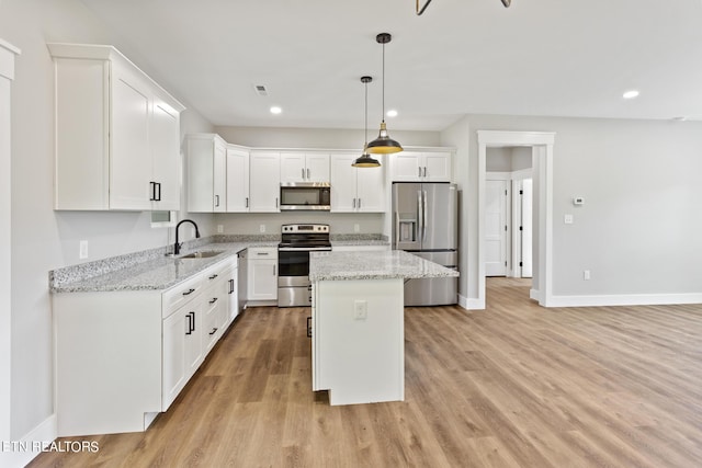 kitchen with appliances with stainless steel finishes, sink, a kitchen island, white cabinetry, and light hardwood / wood-style flooring