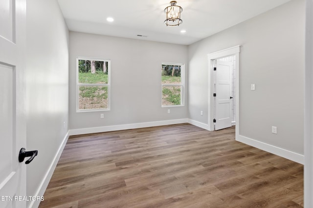 empty room with a notable chandelier, a healthy amount of sunlight, and hardwood / wood-style flooring