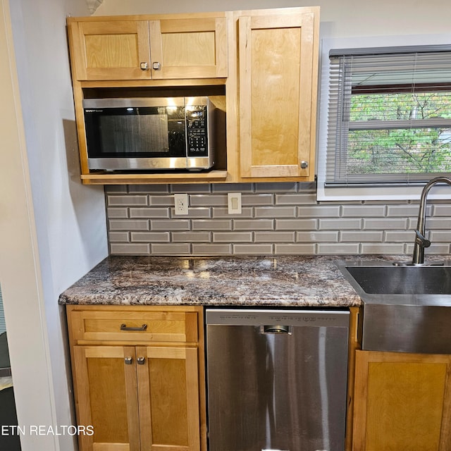 kitchen featuring stainless steel appliances, backsplash, dark stone countertops, and sink