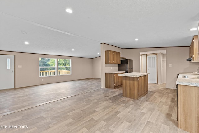 kitchen featuring sink, a textured ceiling, stainless steel refrigerator, a center island, and light hardwood / wood-style floors