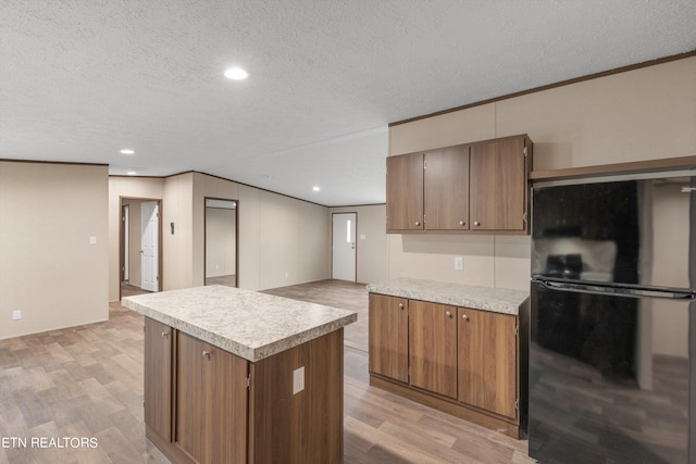 kitchen featuring light wood-type flooring, a textured ceiling, a kitchen island, crown molding, and black refrigerator