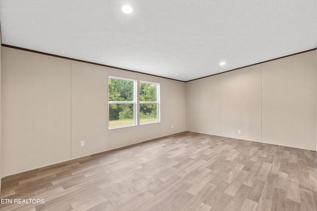 empty room with ornamental molding, light wood-type flooring, and a textured ceiling