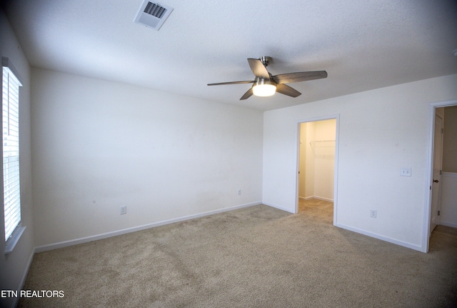 unfurnished bedroom featuring a spacious closet, a closet, ceiling fan, and light colored carpet