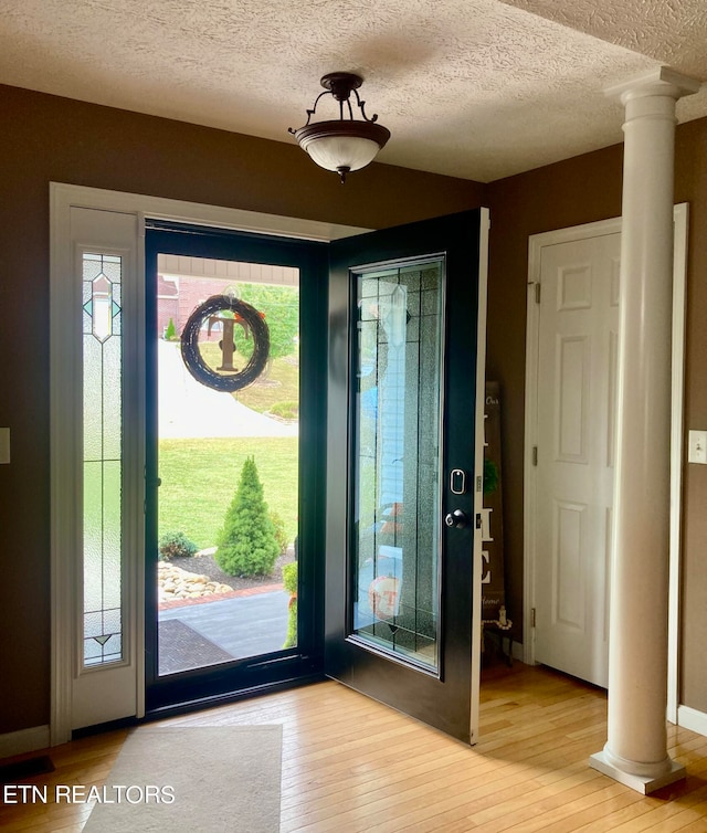 entrance foyer with a textured ceiling, light hardwood / wood-style floors, and ornate columns