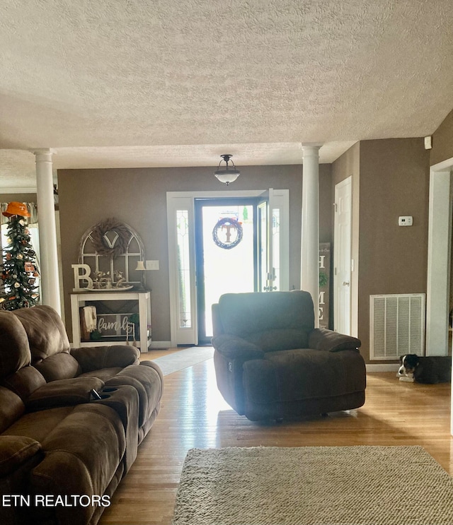 living room with a textured ceiling, light wood-type flooring, and decorative columns