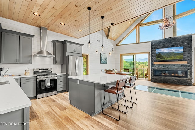 kitchen featuring high vaulted ceiling, gray cabinets, stainless steel appliances, decorative light fixtures, and wall chimney range hood