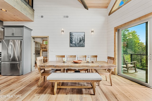 dining room with high vaulted ceiling, wooden walls, beam ceiling, and light hardwood / wood-style flooring