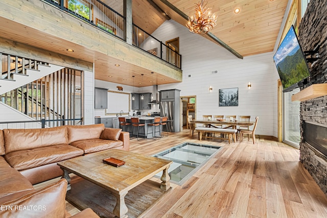 living room featuring high vaulted ceiling, a fireplace, beam ceiling, hardwood / wood-style floors, and a notable chandelier