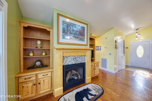 living room featuring a tiled fireplace, vaulted ceiling, and hardwood / wood-style floors