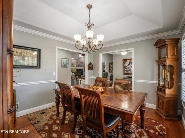 dining space with a raised ceiling, ornamental molding, dark wood-type flooring, and a notable chandelier