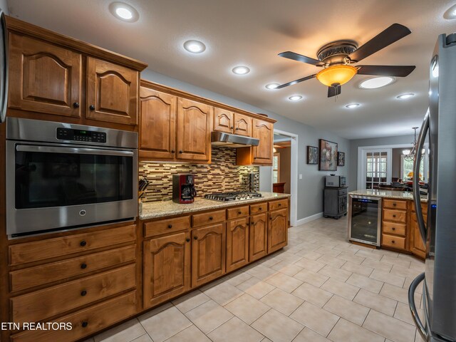 kitchen featuring light stone counters, tasteful backsplash, stainless steel appliances, beverage cooler, and ceiling fan